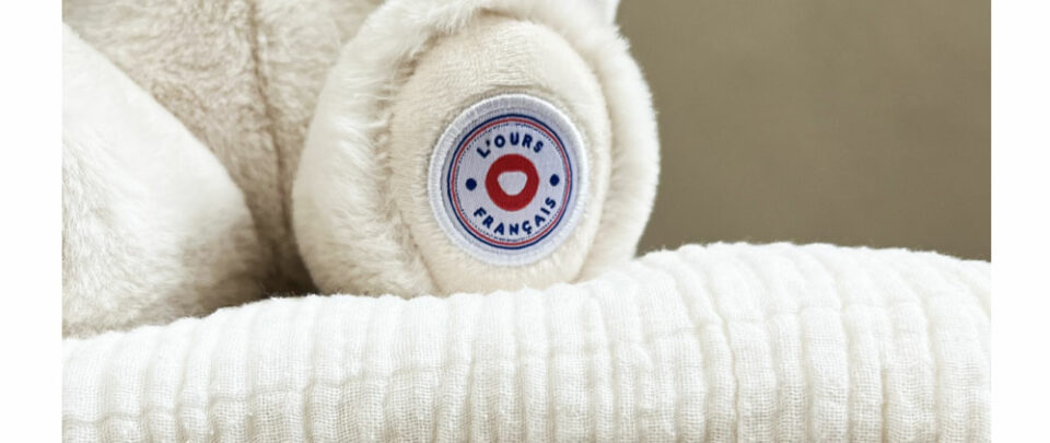 macaron logo de l'ours français sur la patte d'un ours en peluche ours français